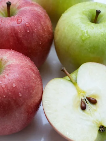 Manzanas rojas y verdes frescas sobre tabla, cortadas y enteras, con zumo