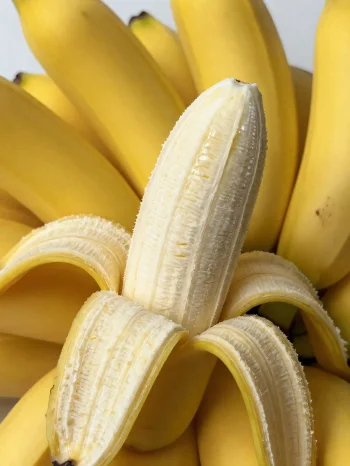 Plátano fresco entero y en rodajas, en cuenco y sobre mesa rústica