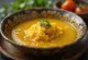 Rasam servido en caldo rico y especiado con pulpa de grosella y hojas de cilantro frescas